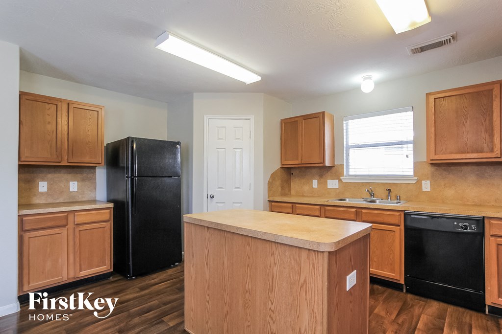 an empty kitchen with wooden cabinets and a black refrigerator