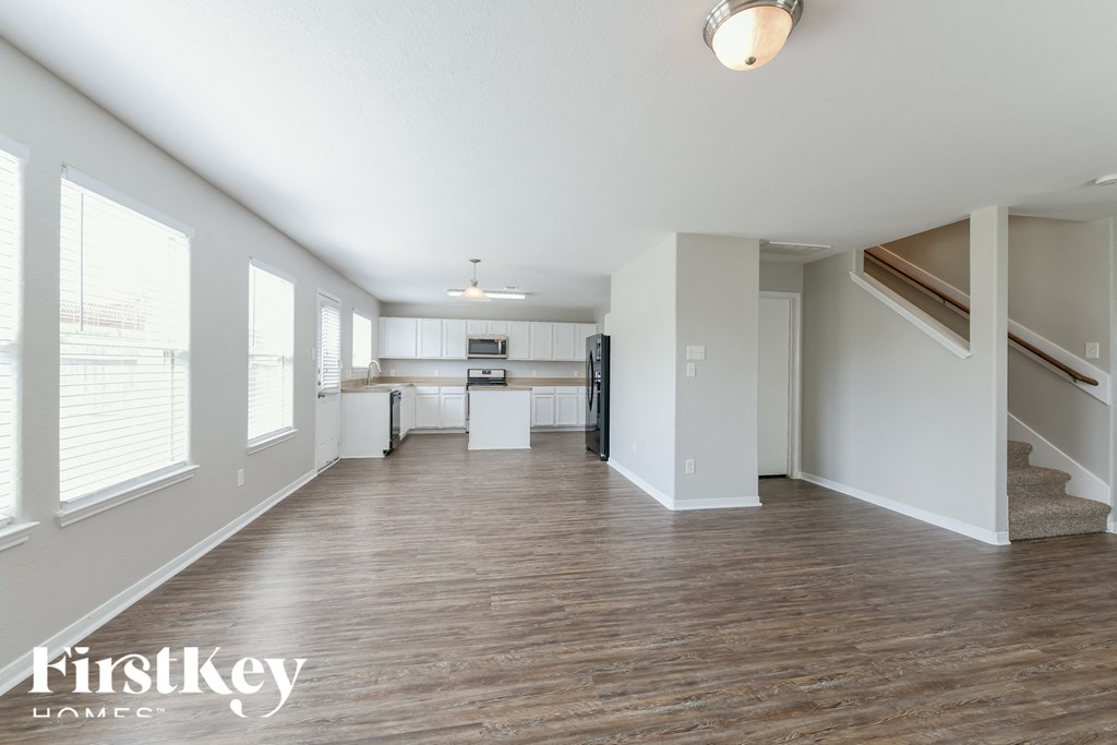 an empty living room with a staircase and a kitchen