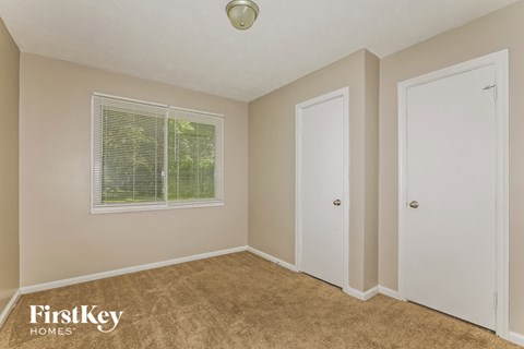 a bedroom with beige carpet and a window and white doors