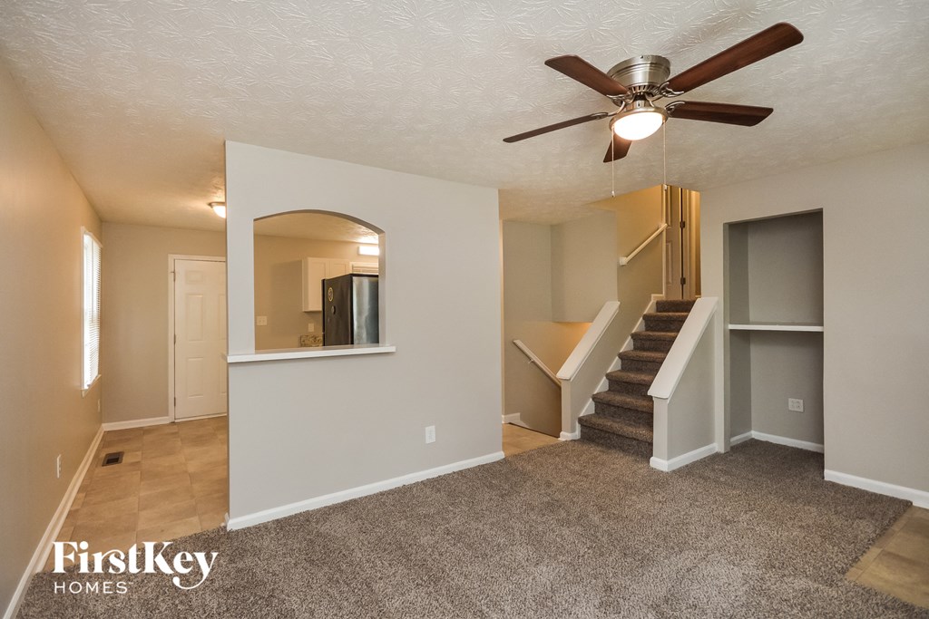 an empty living room with a ceiling fan and a staircase