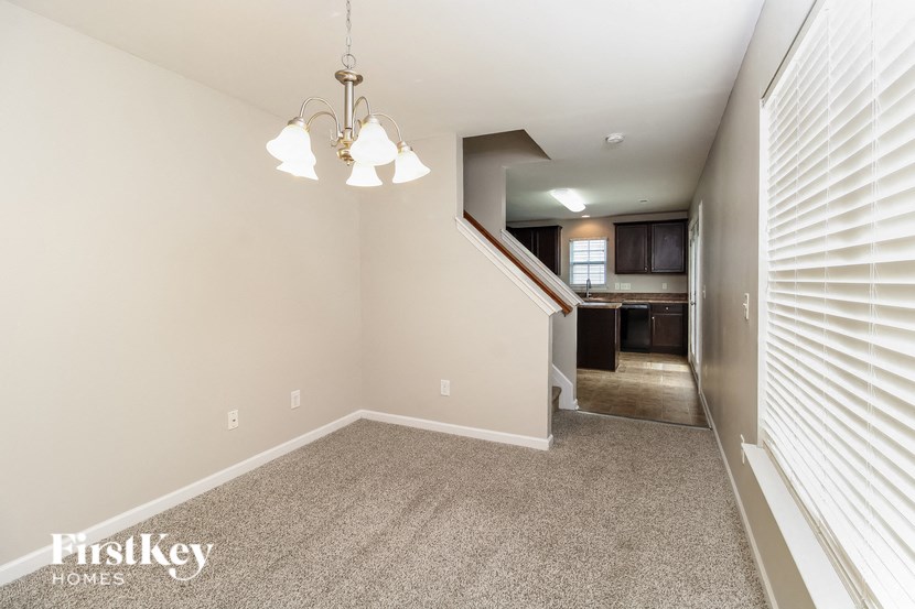 A well-lit, empty room with a staircase leading to the kitchen.
