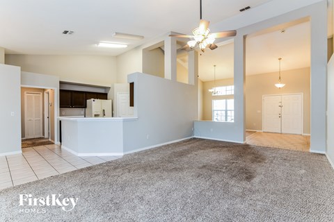 A spacious living room with a grey carpet and a FirstKey Homes logo.