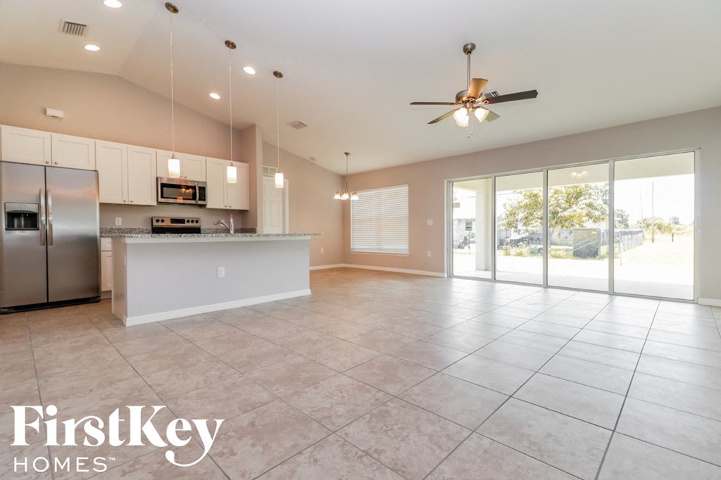 an empty living room with a kitchen and a ceiling fan