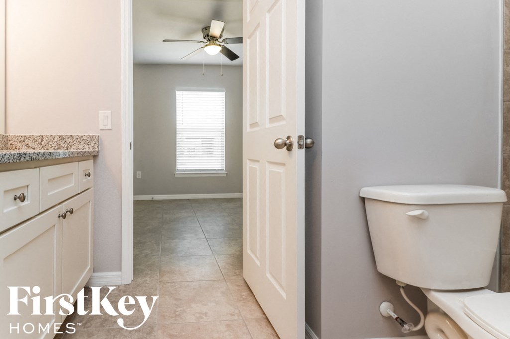 a white bathroom with a toilet and a ceiling fan