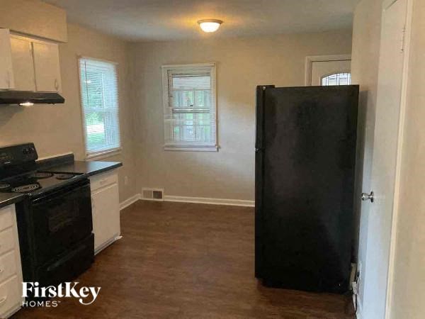 A black refrigerator stands in a kitchen with white cabinets and a stove.