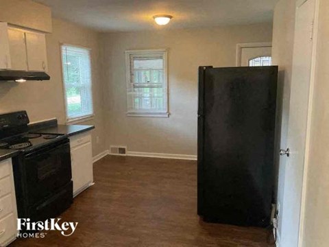 A black refrigerator stands in a kitchen with white cabinets and a stove.