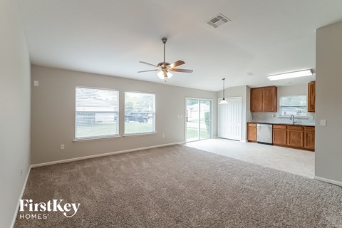 an empty living room with a ceiling fan and a kitchen