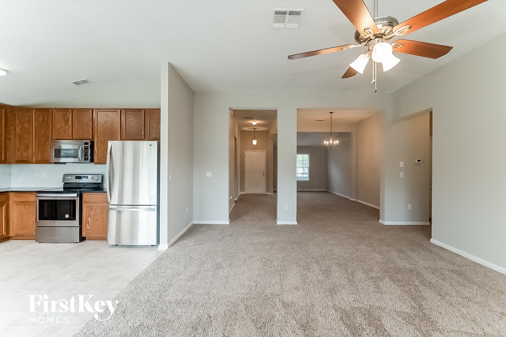 an empty living room with a kitchen and a ceiling fan