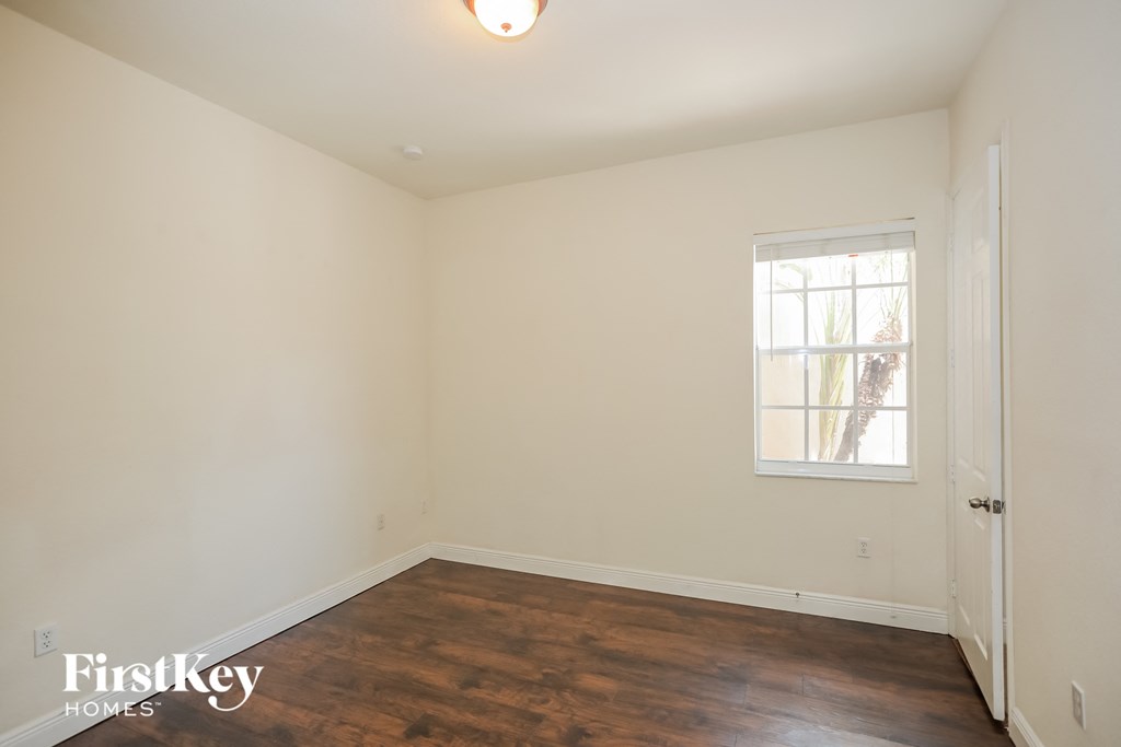 a bedroom with white walls and wood floors and a window