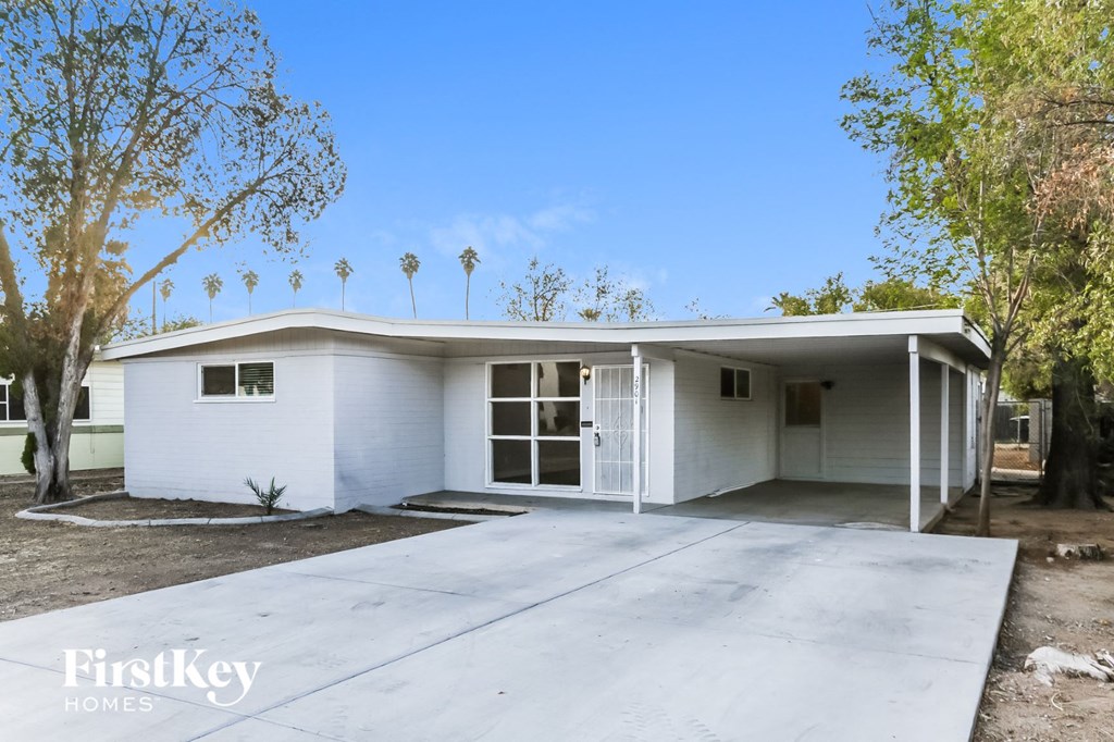 a small white house with a driveway and trees