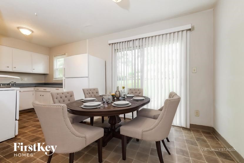 A dining room with a table set for four and chairs around it.