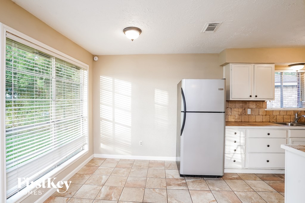 A kitchen with a white refrigerator and white cabinets.