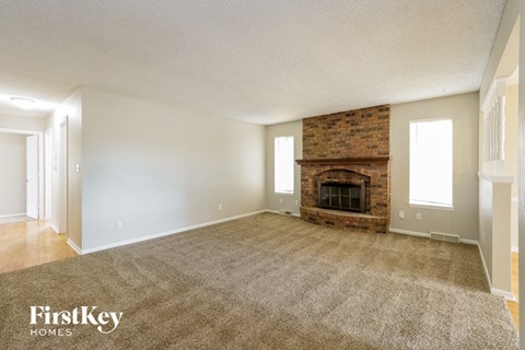 an empty living room with a brick fireplace and carpeting
