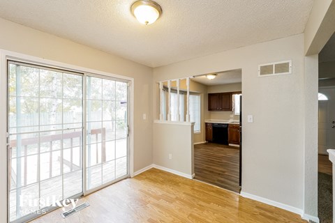 an empty living room with a sliding glass door to a kitchen