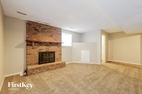 an empty living room with a brick fireplace and carpeting