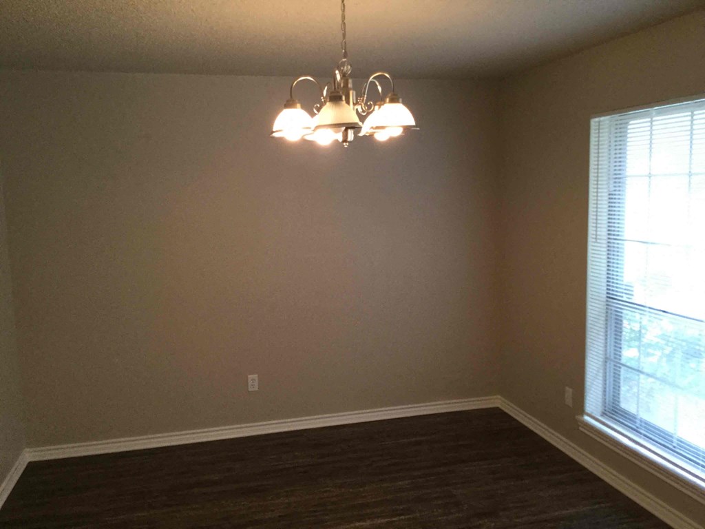 A chandelier hangs over a wooden floor in a room with a window.
