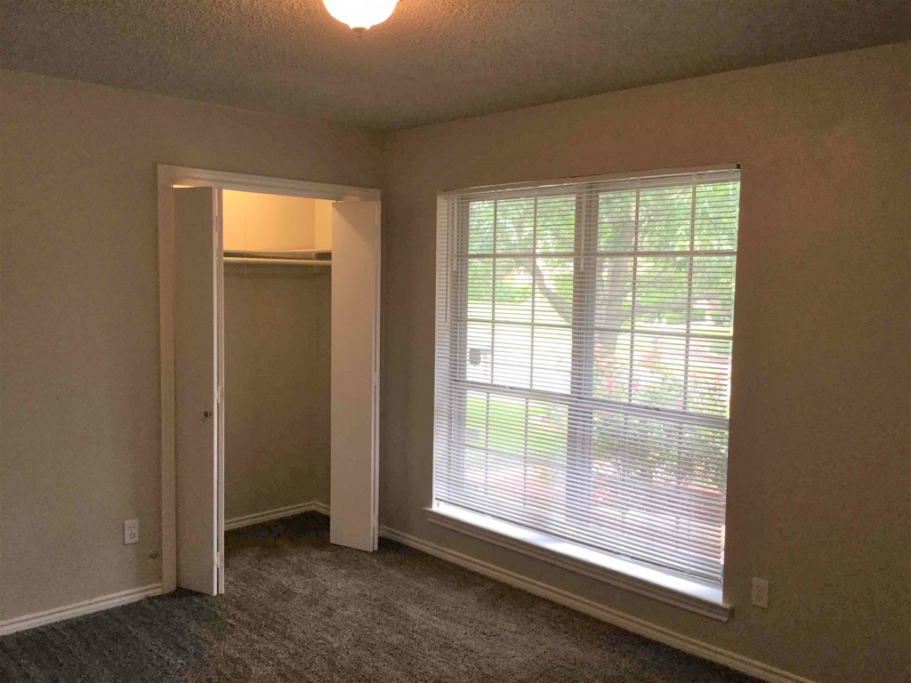 A room with a carpeted floor and a window with blinds.