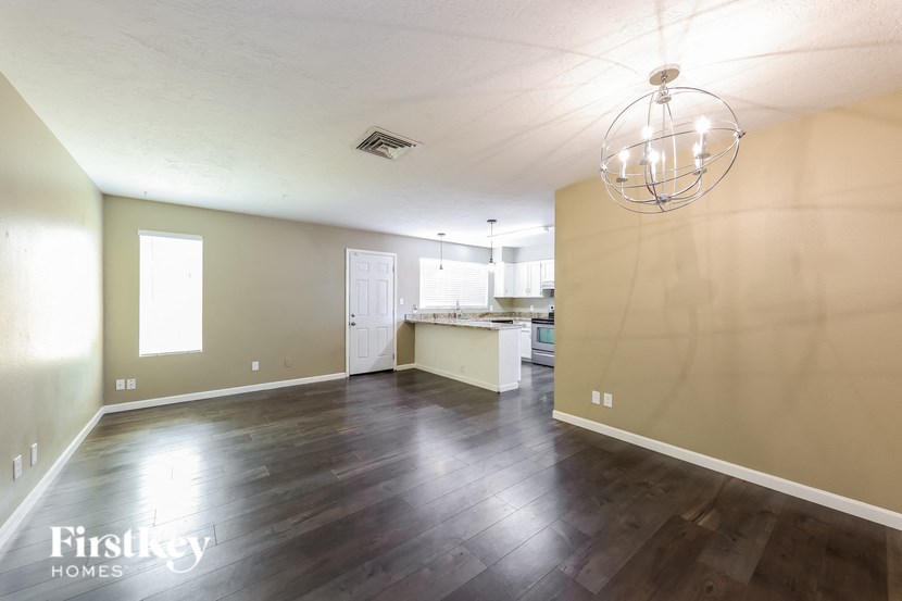 an empty living room and kitchen with wood floors and a chandelier