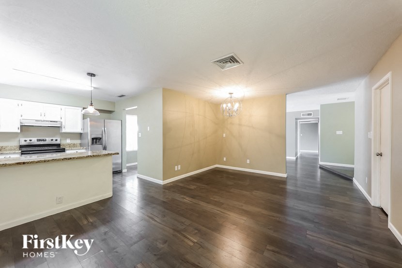 an empty living room and kitchen with wood flooring and white walls