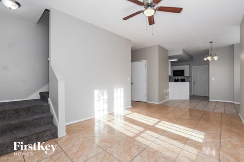 A spacious living room with a staircase and a ceiling fan.