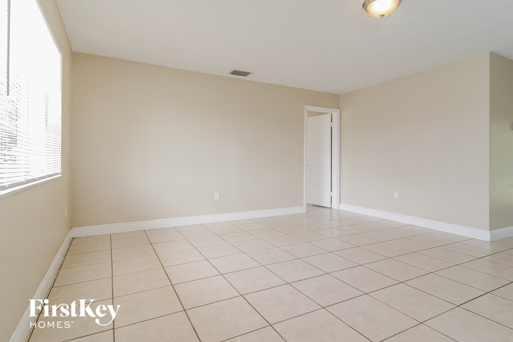an empty living room with a large tiled floor and a door to a hallway