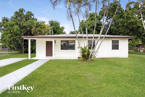 a small white house with a lawn and palm tree