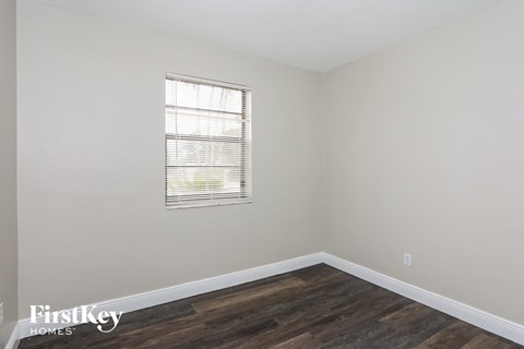 a bedroom with white walls and wood floors and a window