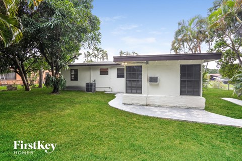 a small white house with a grassy yard and palm trees