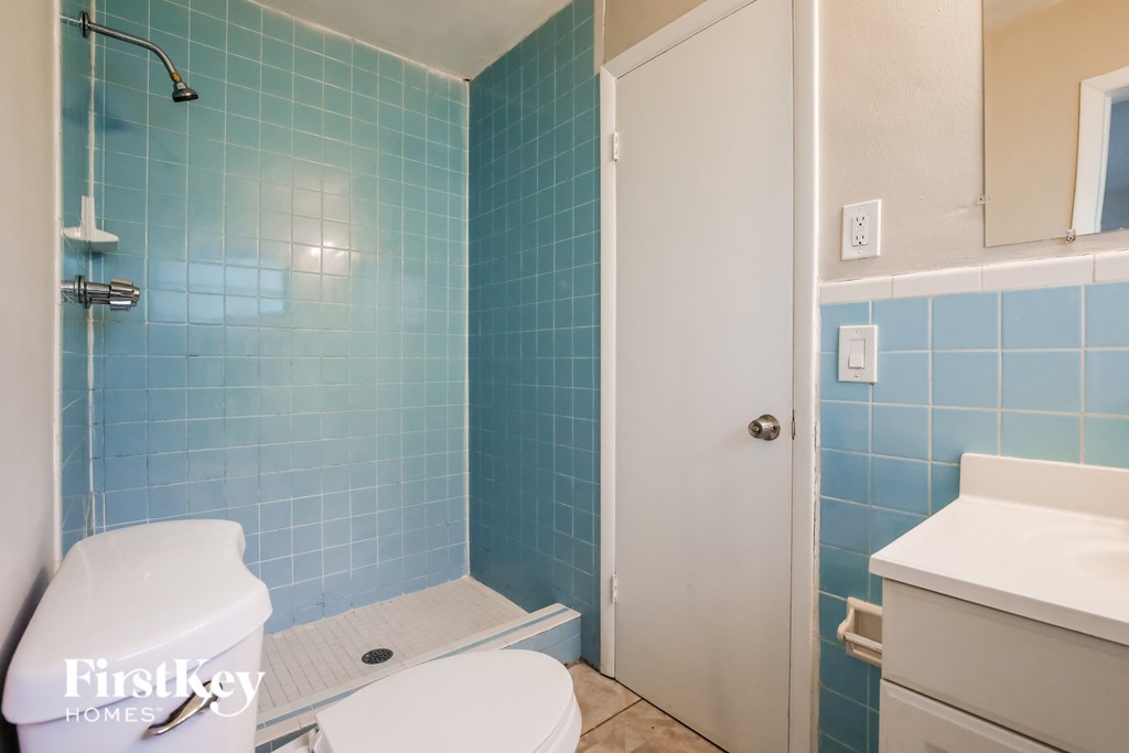 a bathroom with blue tile and a white toilet and shower