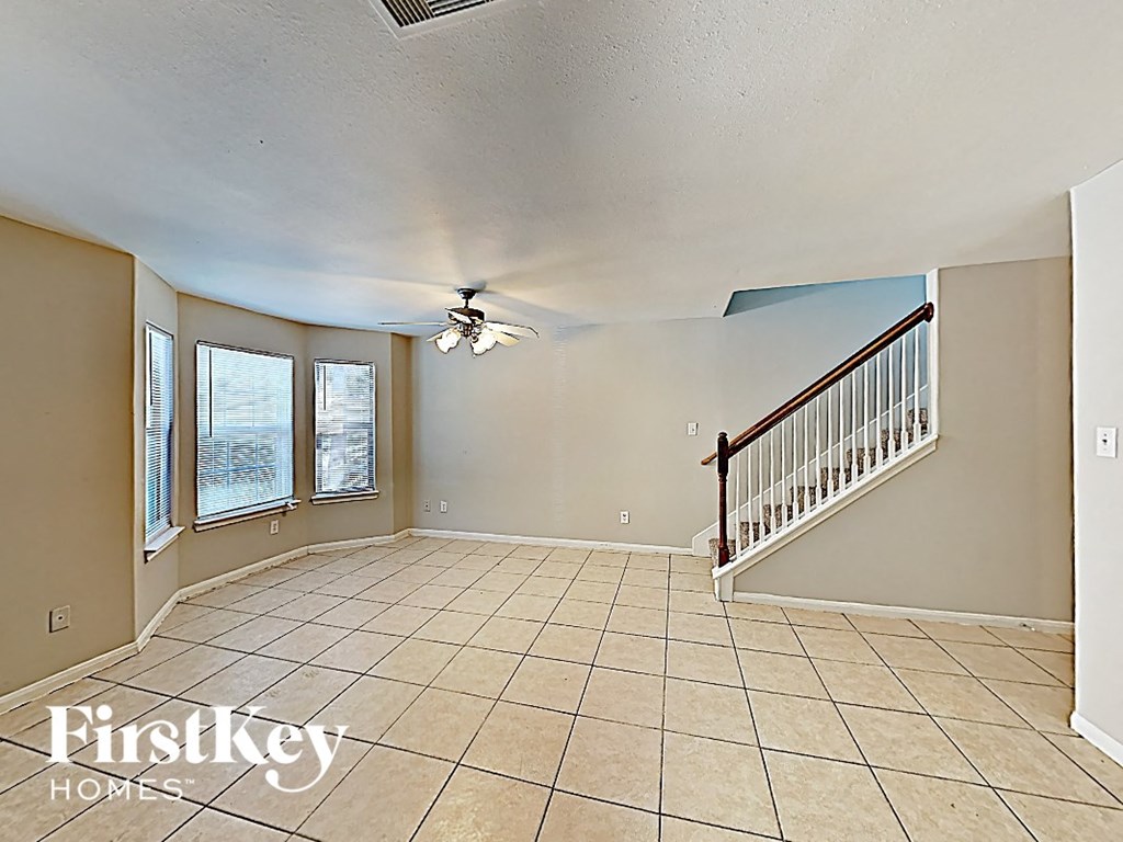 an empty living room with a ceiling fan and a staircase