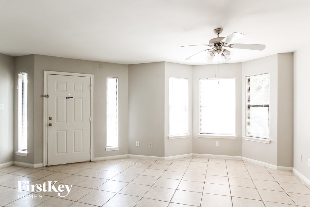 an empty living room with a ceiling fan and three windows