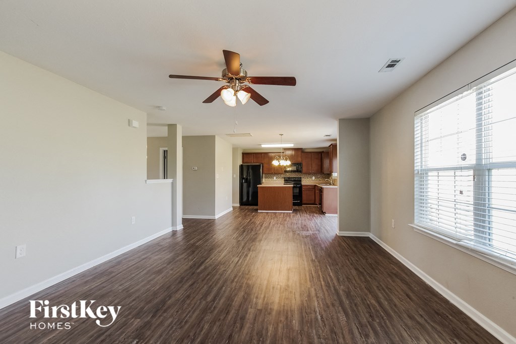 an empty living room with a ceiling fan and a kitchen