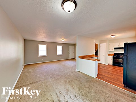 A spacious room with a carpeted floor and a kitchen area in the background.