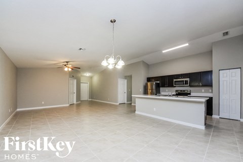 A spacious kitchen and living room with a white ceiling and tiled floor.