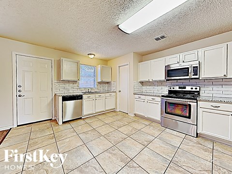 A kitchen with white cabinets and appliances, a tiled floor, and a window.