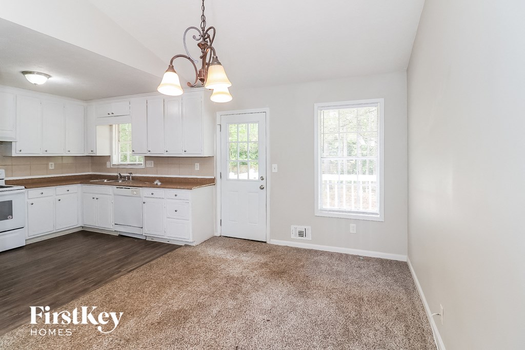 a kitchen with white cabinets and white appliances and a carpeted floor