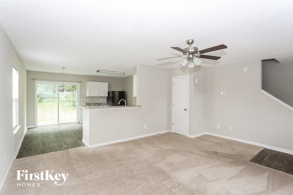 an empty living room with a ceiling fan and a kitchen