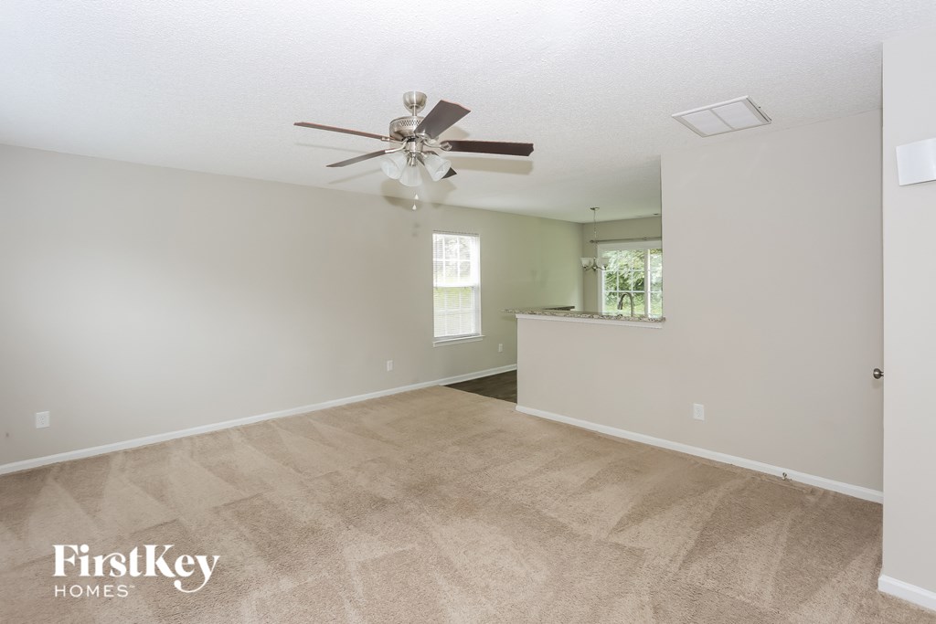 the living room and dining room of a house with carpet and a ceiling fan