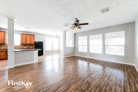 an empty living room with a ceiling fan and a kitchen