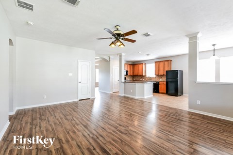 an empty living room with a ceiling fan and a kitchen