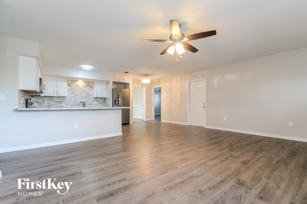 an empty living room with a ceiling fan and a kitchen