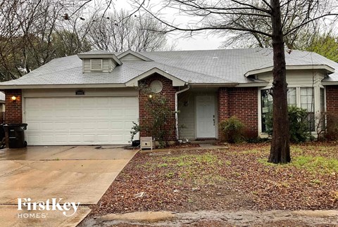 A brick house with a garage door and a tree in front.