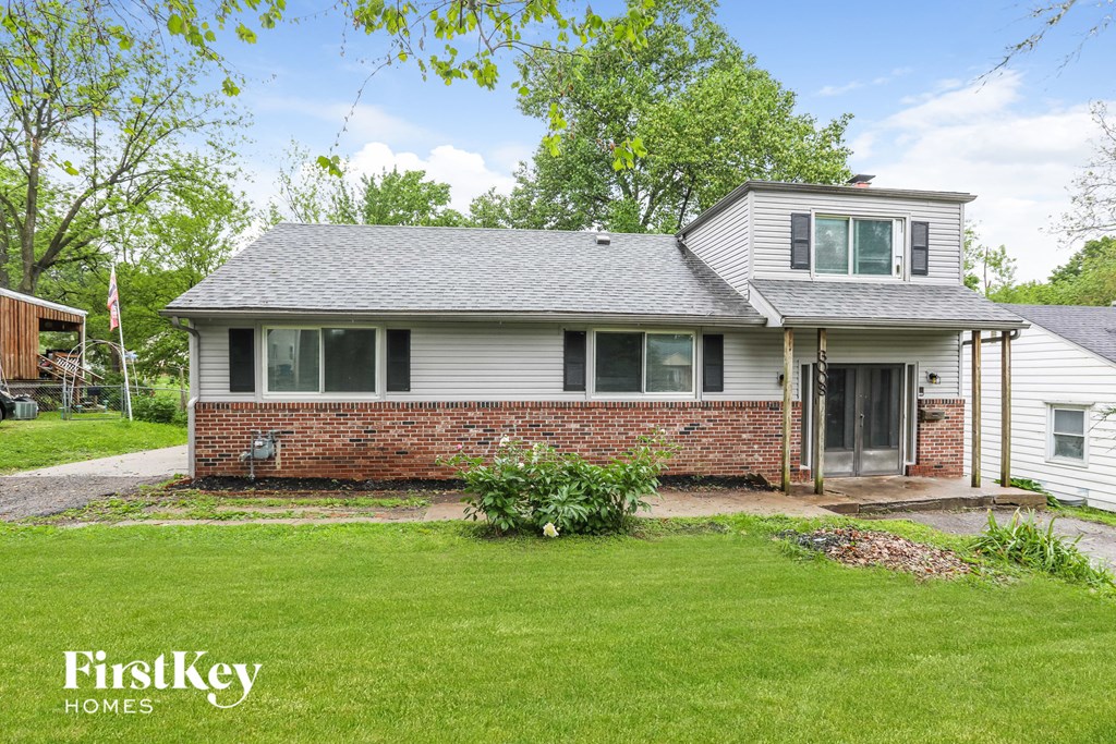 A house with a grey roof and a brick wall is for sale.