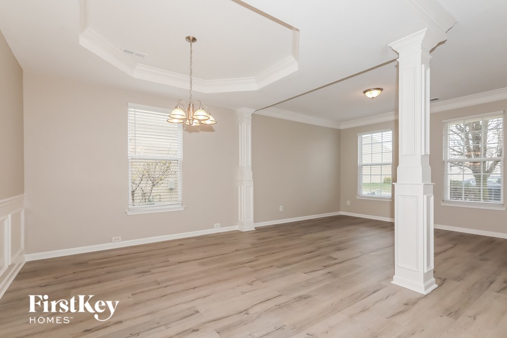 the living room of a home with white pillars and wood flooring