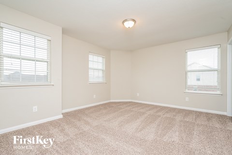 a spacious living room with carpet and two windows