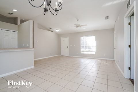 an empty living room with a kitchen and a ceiling fan
