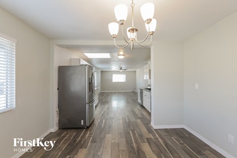 the living room and kitchen of an apartment with a refrigerator and a chandelier