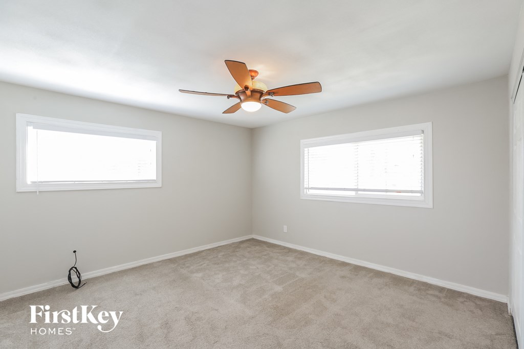 a bedroom with a ceiling fan and two windows