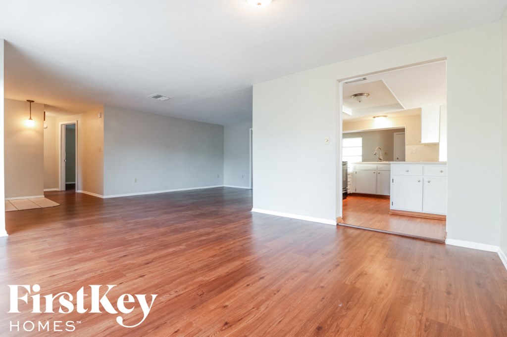 an empty living room and kitchen with wood floors and white walls