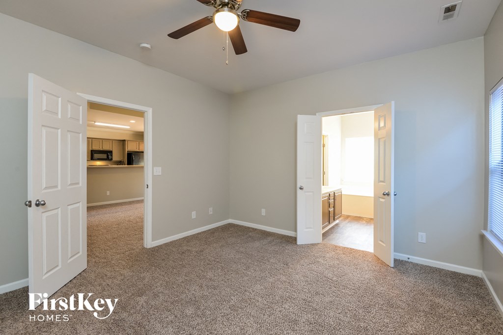 an empty living room with a ceiling fan and a door to a kitchen